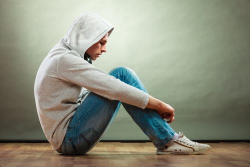 man sitting with hood on displaying one type of PTSD