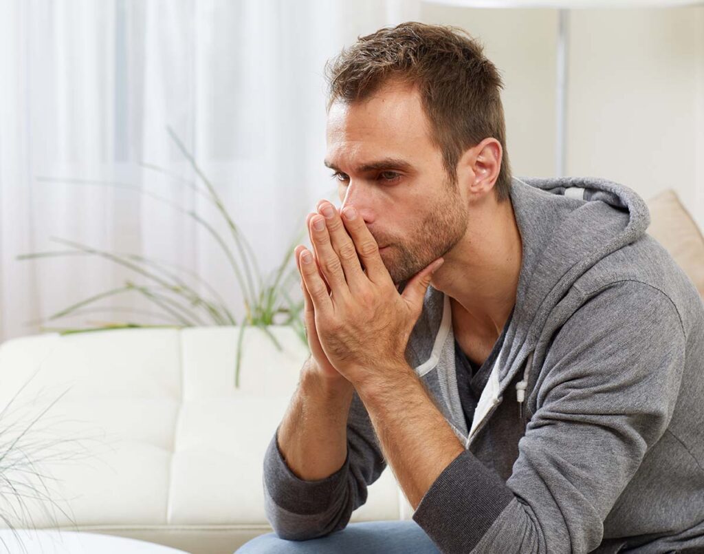 Man sits on couch and puts head in hands as struggles with how do deal with ADHD