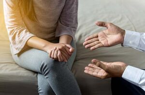 Client sits on couch and holds hands together while talking to therapist during psychotherapy in CA