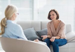 Woman sits on couch and talks to client in a mental health treatment center